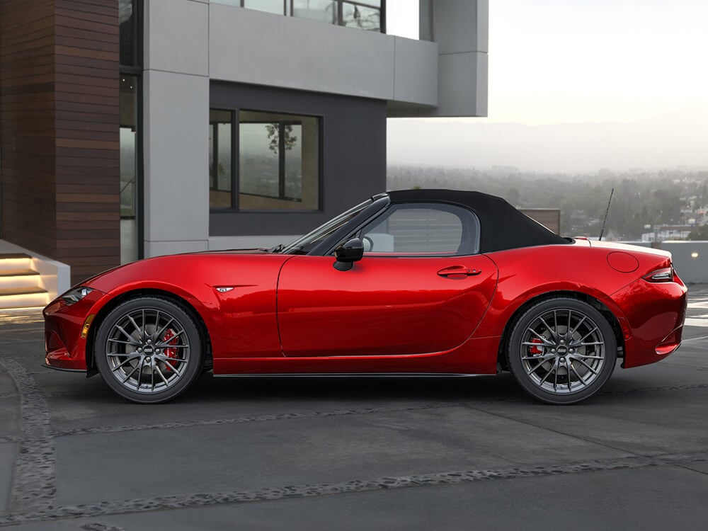 Side view of a red MX-5 ST parked in front of a modern home with its top up.
