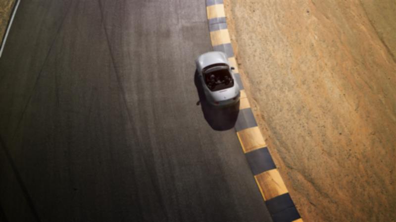 A top-down view of an MX-5 ST as it drives on a road next to sandy terrain.