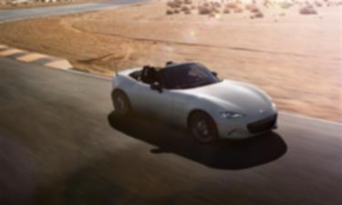 An MX-5 ST with its top down drives down a desert road next to sandy terrain.