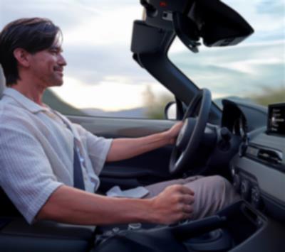 A person smiles while driving an MX-5 ST with the top down.