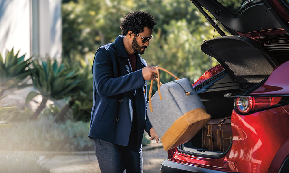 Un homme retire des bagages du coffre ouvert d'une Mazda CX-30 rouge cristal métallisé.