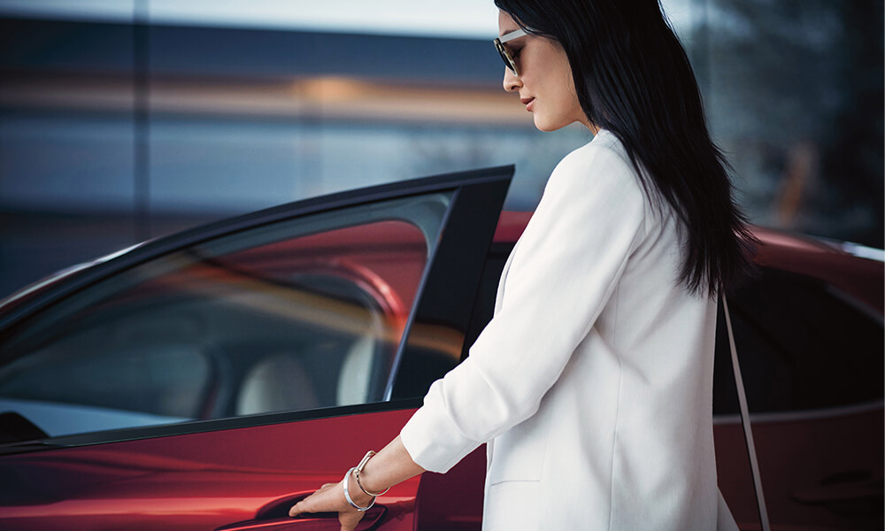 Une femme ouvre la portière côté conducteur d’un Mazda CX-30 rouge vibrant cristal métallisé