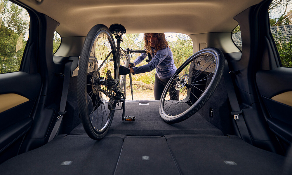 View from the back seats of a Mazda CX-5, showing a woman loading a bicycle with the rear seats fully folded down.