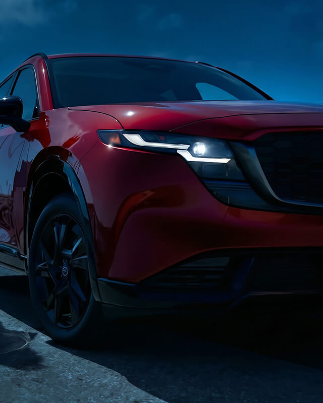 Low-angle front corner view of a Mazda CX-5 against a dark blue sky.