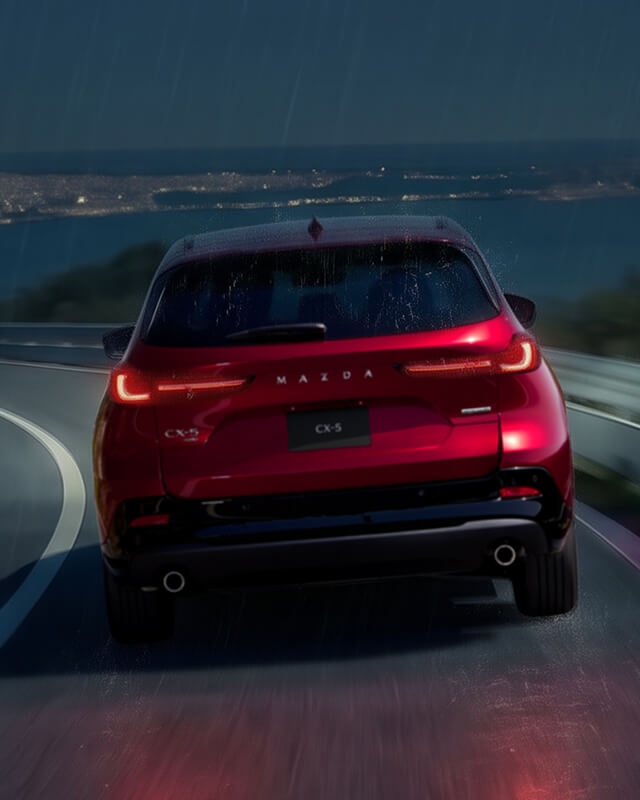 Rear view of a Mazda CX-5 driving on a winding road at night.