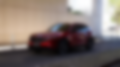 A Soul Red Crystal Mazda CX-5 shown from the front side profile, with a blurred city road in the background.