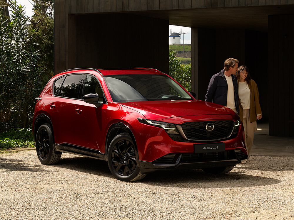 Profil latéral avant d'un Mazda CX-5 rouge vibrant cristal garé dans une allée avec un homme et une femme debout à côté.