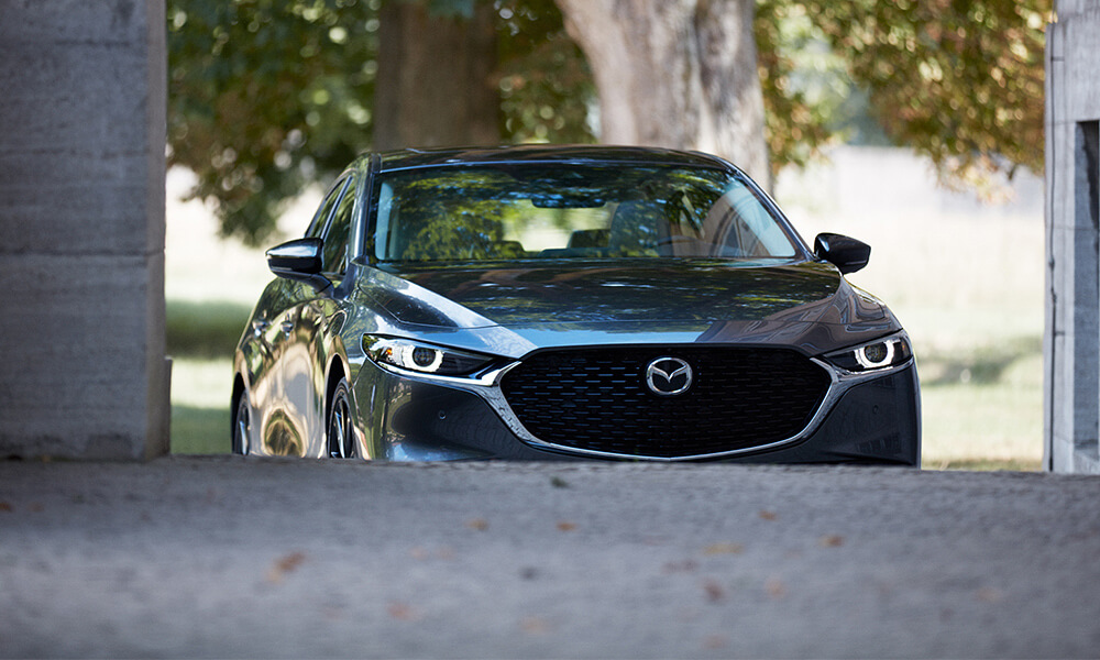 Front view of a Deep Crystal Blue Mica Mazda3, with the front wheels partially obscured by the road, appearing to drive up a hill.