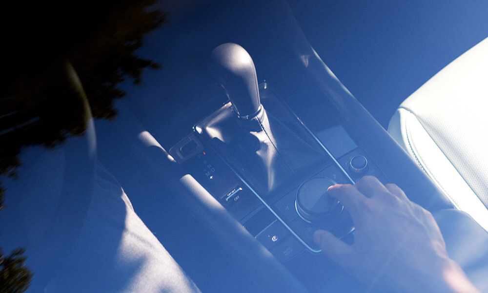 View through the panoramic moonroof of a Mazda3, looking down at a hand resting on the centre control knob.